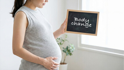 Pregnant woman holding a chalkboard with text body change in bright room, expectant mother embracing pregnancy journey transformation, maternity and motherhood lifestyle health wellness concept