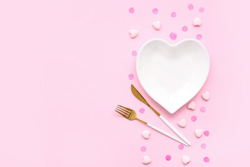 Table setting for Valentine's Day with confetti and decorative hearts on pink background