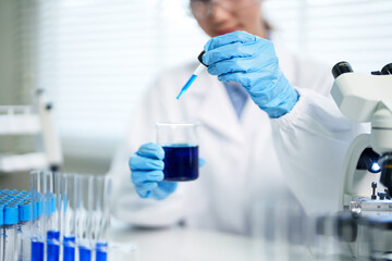 Adult scientist performing chemical experiment in laboratory using dropper transferring blue liquid...