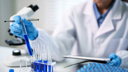 Adult scientist researcher professional conducts chemical analysis experiment utilizing test tubes microscope tablet inside laboratory research facility
