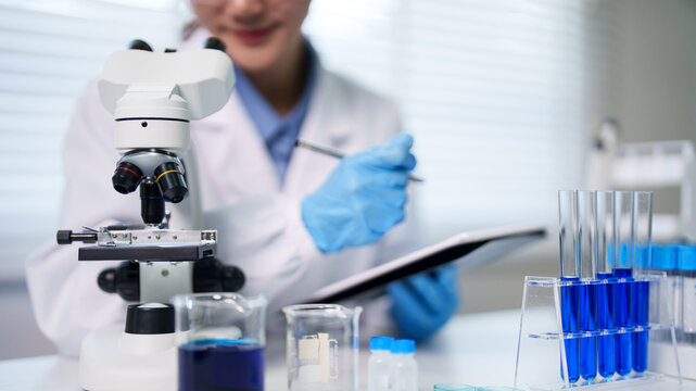 Asian adult scientist conducting laboratory research using microscope recording data discovering new solutions in modern lab environment for medical innovation