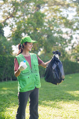 Adult Asian woman volunteer collects plastic bottle trash in park promoting environmental sustainability community service outdoors