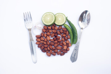 Minimalist food scene featuring raw peanuts arranged with lime half slices, onion rings, and fresh green chilies between silver forks and a spoon.