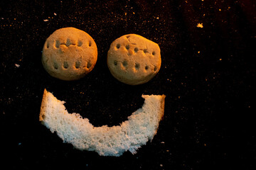Smiling Bread Face With Two Round Cookies as Eyes and Crescent Slice Mouth on Dark Surface