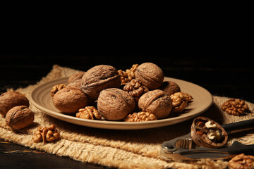 Plate with tasty walnuts and nutcracker on black wooden table against dark background