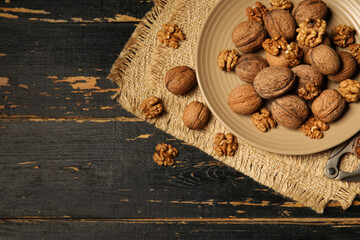Plate with tasty walnuts and nutcracker on black wooden background