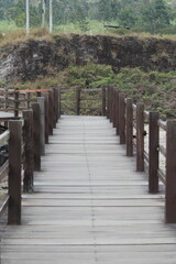 A wooden boardwalk with railings leading to a rocky cliff with lush greenery