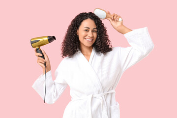 Beautiful young African-American woman with modern hair dryer and brush on pink background