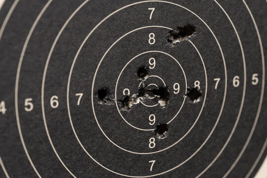 Close up of a black paper shooting target with multiple bullet holes in the center bullseye after target practice session.