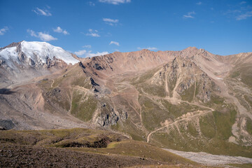 Winding gravel road in the high mountains of Tien Shan with a view of the massive Tuyuksu glacier. Remote alpine landscape in Central Asia