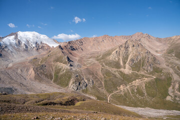 Winding gravel road in the high mountains of Tien Shan with a view of the massive Tuyuksu glacier. Remote alpine landscape in Central Asia