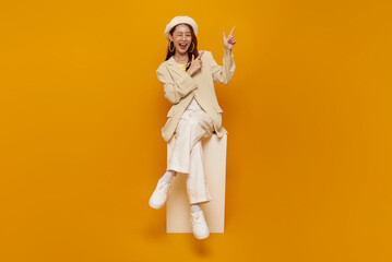 Playful advertising presentation concept with Asian woman sitting and pointing upward while smiling and winking to highlight creative idea promotion message positive energy lifestyle content.