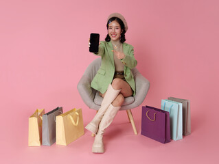 Online shopping mobile app promotion Asian woman sitting on chair holding smartphone with blank screen showcasing ecommerce marketing digital retail experience and lifestyle shopping concept