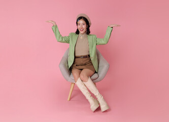 Lifestyle presentation portrait smiling Asian woman sitting on chair with open hands gesture comparison and choice concept marketing presentation decision making pink studio background.