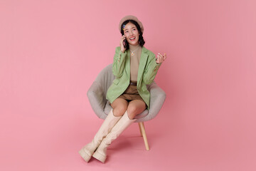 Lifestyle communication portrait smiling Asian woman sitting and talking on smartphone friendly conversation concept online customer service modern digital lifestyle pink studio background.