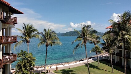 Fototapeta premium A scenic tropical beach view with palm trees, turquoise ocean water, and resort buildings along the shoreline.
