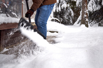 Man shoveling snow in a backyard during winter, clearing a path near a house. Snowy weather, warm clothing, seasonal outdoor work and home maintenance in cold climate