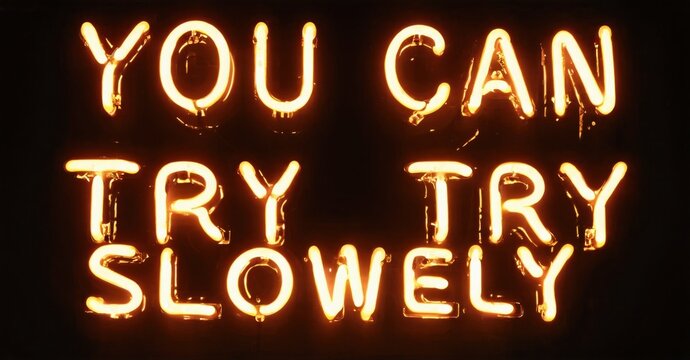 Bright neon sign displays text. Words read You Can Try Try Slowly. Dark background emphasizes glowing letters. Simple, motivational message. - Powered by Adobe