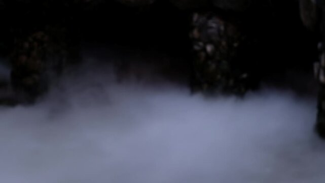 Mysterious fog swirling around ancient stone structures in darkness