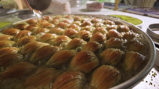 Close-up 10-bit slow motion of hot syrup poured on golden midye baklava. Showcasing the unique mussel-shaped pastry and sizzling syrup in a professional Gaziantep bakery. 4K quality.