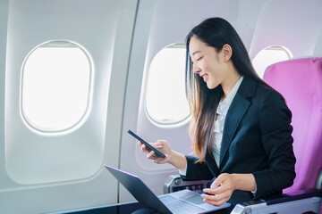  A woman is sitting on an airplane, working and looking at her laptop.