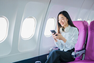 Fototapeta premium The businesswoman enjoyed her flight by listening to music with wireless headphones and using her smartphone while on the plane.