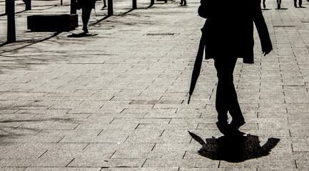 Minimalist monochrome silhouette of a faceless shadow with an umbrella reflecting on the ground.