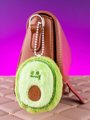 Close-up of a soft plush keychain in the shape of a green avocado on a brown  bag.