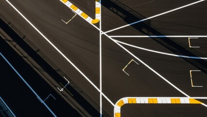 Aerial view of a racetrack featuring white lines yellowwhite safety barriers and shadows creating stark contrasts on the asphalt surface