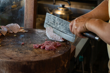 Vietnamese pho bo beef preparation with chef slicing meat on wooden board