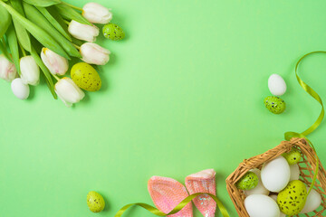 Easter holiday concept with easter eggs, basket and white tulip flowers on green background. Top view, flat lay