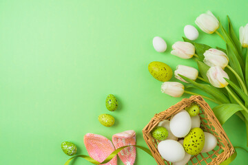 Easter holiday concept with easter eggs, basket and white tulip flowers on green background. Top view, flat lay