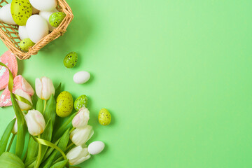 Easter holiday concept with easter eggs, basket and white tulip flowers on green background. Top view, flat lay