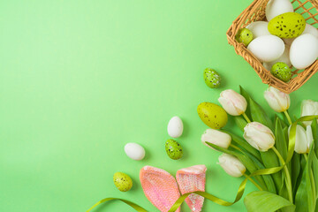 Easter holiday concept with easter eggs, basket and white tulip flowers on green background. Top view, flat lay