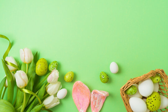 Easter holiday concept with easter eggs, basket and white tulip flowers on green background. Top view, flat lay