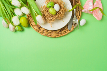 Easter festive table setting with easter eggs decoration and white tulips flowers on green background. Top view , flat lay