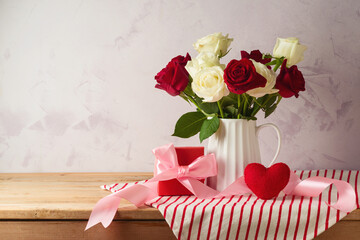 Happy Valentine's day concept with rose flowers, gift box, bow and heart shape on wooden table over bright background