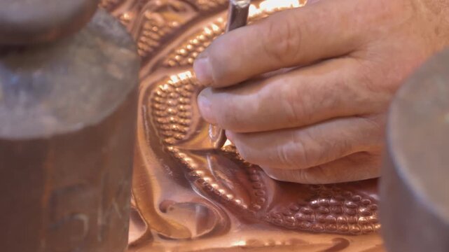 Artisan hand-engraving a traditional copper plate with hammer and chisel. Intricate patterns and rhythmic craftsmanship in a Turkish metalwork shop. 10-bit 4K slow motion.