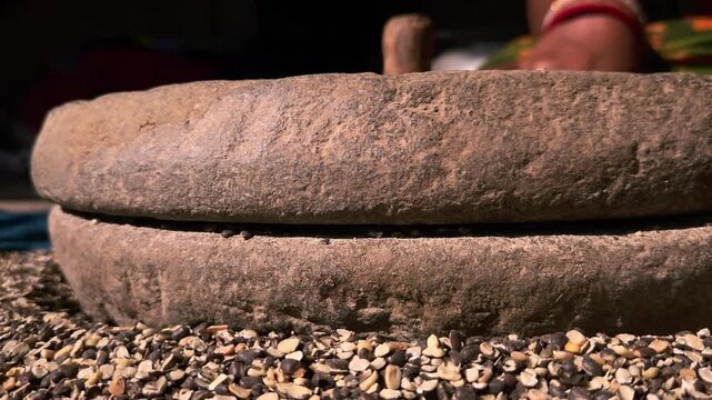 Indian woman in a rural setting using a traditional hand-operated millstone, also known as a quern, to grind Black gram lentils.