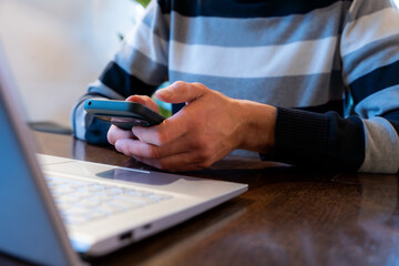 Person Scrolling Smartphone During Work Break, Checking Social Media Near Laptop At Office Desk, Distraction And Addiction Risk Lowering Productivity. Multitasking Concept
