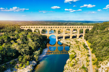 Naklejka premium Aqueduct of Pont du Gard arches over the river, showcasing the rich history of Vers-Pont-du-Gard, France. Ancient aqueduct of Pont du Gard spans the peaceful river in Vers-Pont-du-Gard, France.
