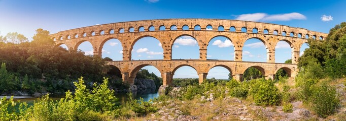 Aqueduct of Pont du Gard arches over the river, showcasing the rich history of Vers-Pont-du-Gard, France. Ancient aqueduct of Pont du Gard spans the peaceful river in Vers-Pont-du-Gard, France.