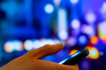 Hand Holding Smartphone In Night City Bokeh Lights, Mobile Browsing And Messaging On The Go, Checking Notifications For Urban Travel, Navigation, And Wireless Connected Lifestyle. Copy Space