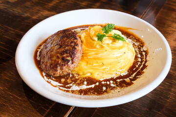 Omelette rice with Hamburger Steak in brown sauce (Omurice) served on a white plate