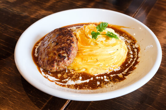 Omelette rice with Hamburger Steak in brown sauce (Omurice) served on a white plate