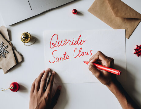 Ni&ntilde;o escribiendo carta a Pap&aacute; Noel en mesa con sobre y material escolar