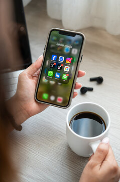 Bangkkok, THAILAND - January 2nd, 2026: hands of woman Iphone with icons of social media on screen place on table with tablet and ear phone and a mug of coffee