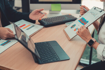 Two accountants use calculators to perform company financial calculations, handle accounting on laptop computers at their desks, manage budgets, and handle financial tasks.