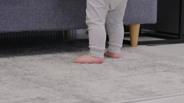 Baby boy takes first steps and learns how to walk barefoot at home. Slow motion