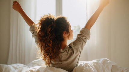Woman stretches in bed while morning light shines through the window in a cozy room
